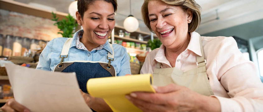 Two cafe owners smiling as they check through the accounts